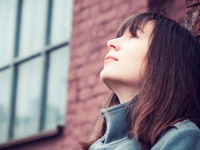 Junge Frau blickt nachdenklich in den Himmel